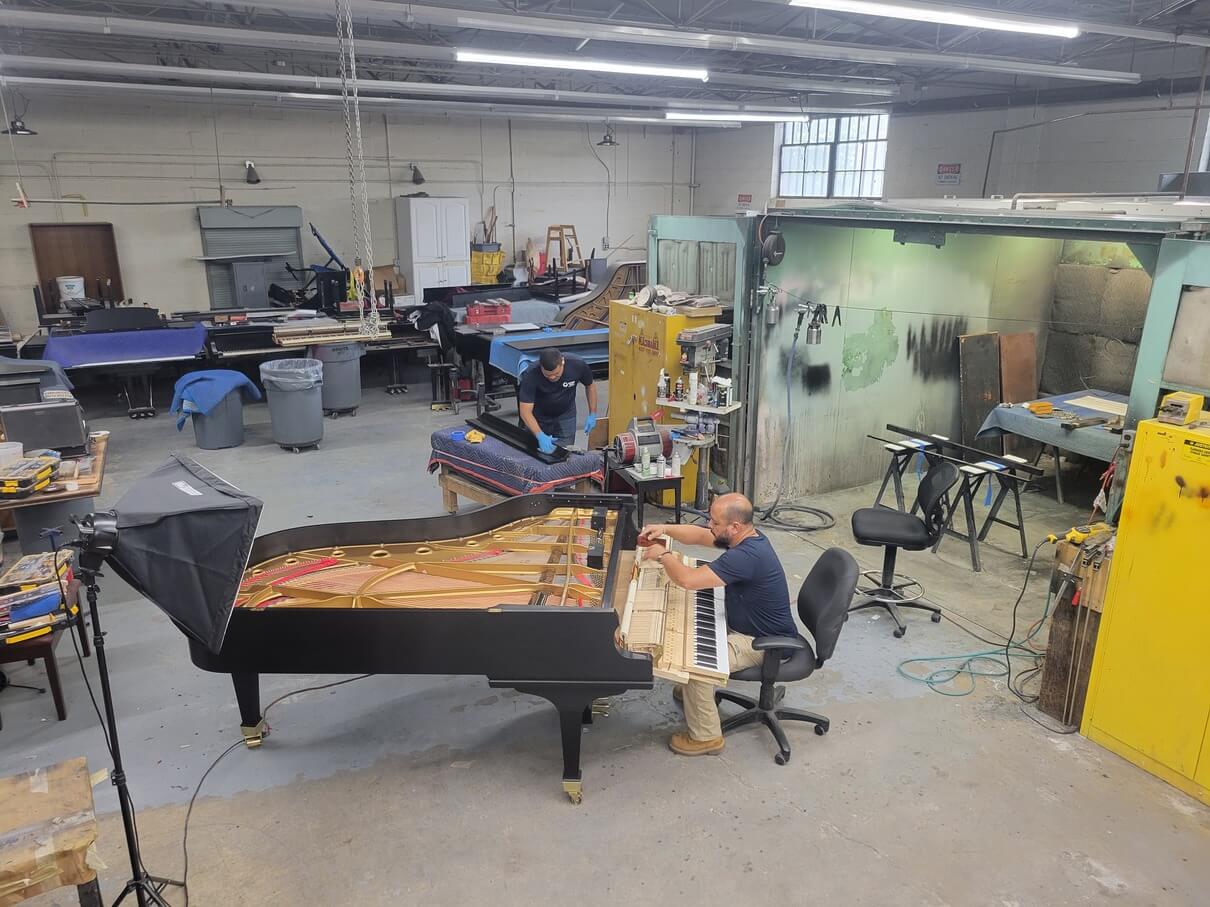 This is an overview of our employees, Jamil & Irving, reconditioning a grand piano, in the back of the shop in the Piano Man Superstore.